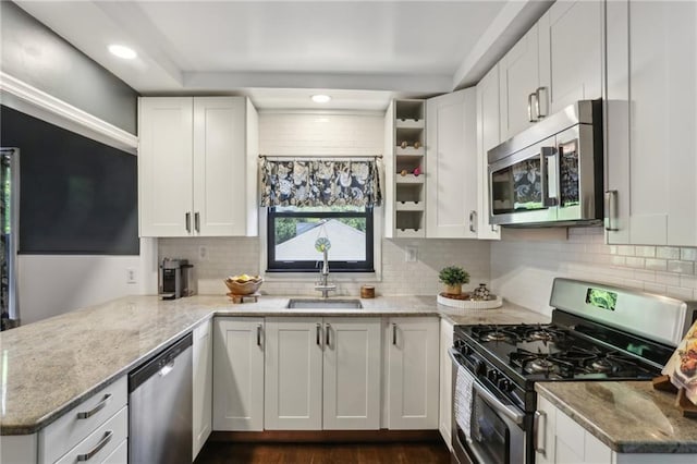 kitchen with appliances with stainless steel finishes, a sink, tasteful backsplash, light stone counters, and white cabinetry