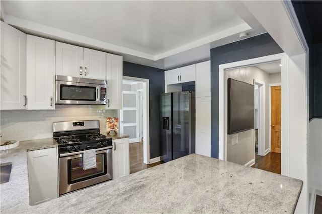 kitchen featuring stainless steel appliances, white cabinetry, backsplash, and dark wood-style floors