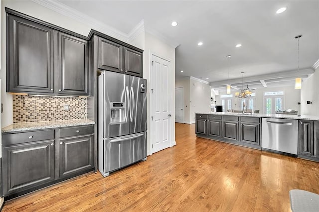 kitchen featuring hanging light fixtures, ornamental molding, appliances with stainless steel finishes, light hardwood / wood-style floors, and light stone counters