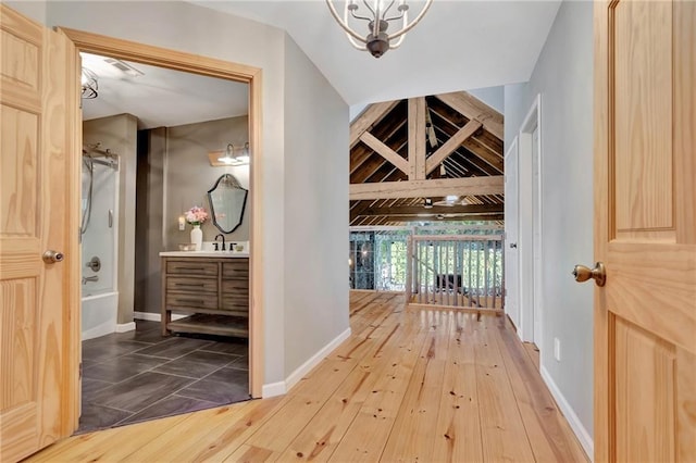 hallway featuring hardwood / wood-style floors, lofted ceiling with beams, and an inviting chandelier