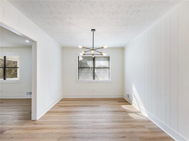 unfurnished dining area featuring a textured ceiling, a notable chandelier, and light wood-type flooring