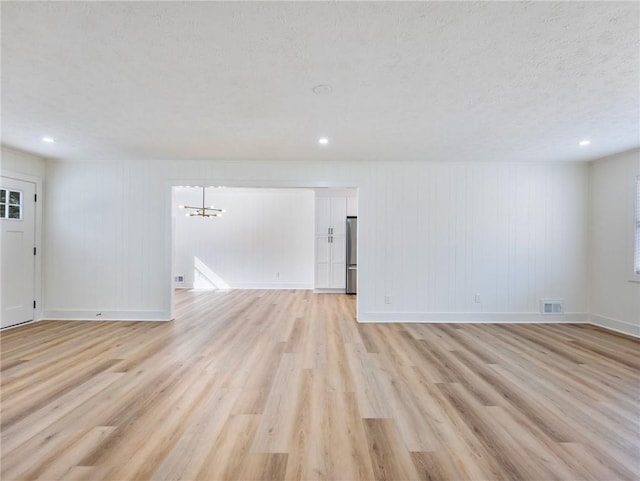 empty room featuring a notable chandelier, a textured ceiling, and light wood-type flooring