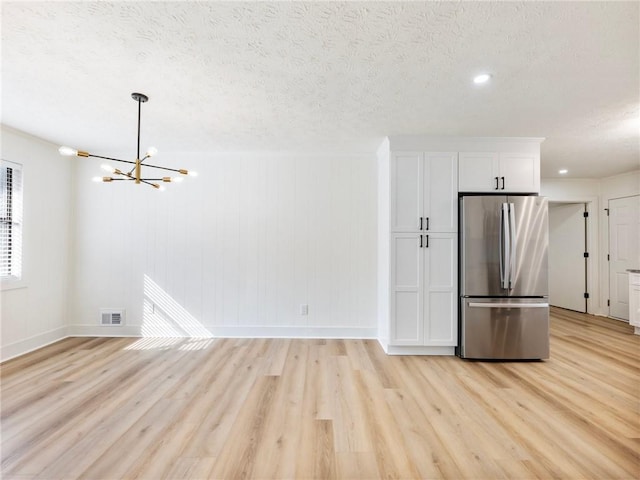 kitchen with stainless steel refrigerator, light wood-type flooring, a textured ceiling, and white cabinets