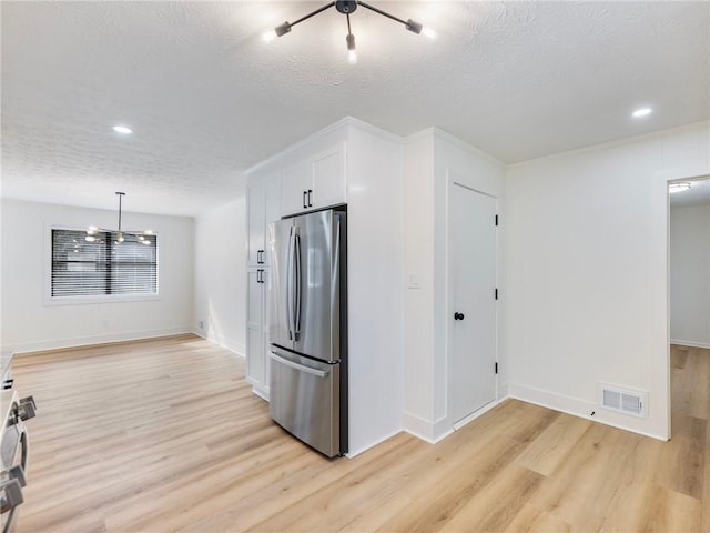 kitchen featuring a textured ceiling, hanging light fixtures, stainless steel refrigerator, light hardwood / wood-style floors, and white cabinets