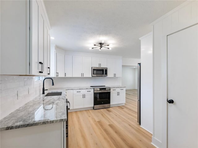 kitchen featuring sink, light hardwood / wood-style flooring, white cabinetry, stainless steel appliances, and light stone counters