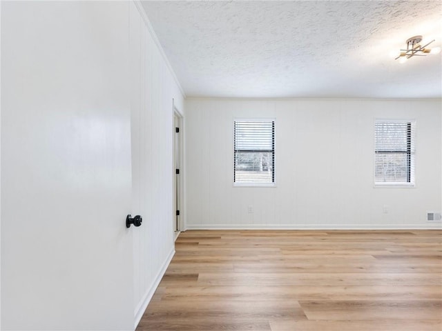 spare room featuring crown molding, a textured ceiling, and light wood-type flooring