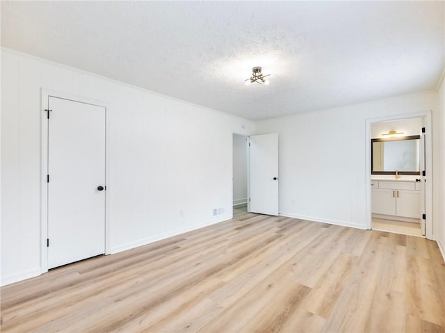 unfurnished bedroom featuring a textured ceiling, light hardwood / wood-style floors, and ensuite bath