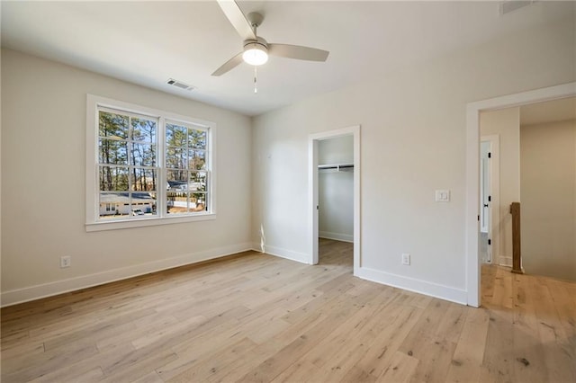 unfurnished bedroom with ceiling fan, a spacious closet, light wood-type flooring, and a closet