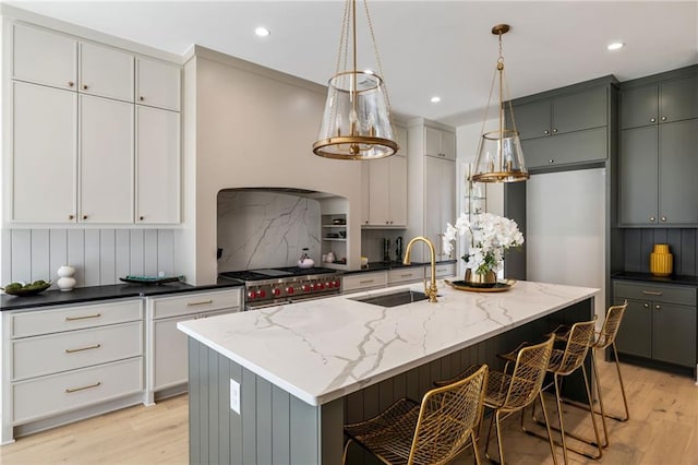 kitchen with sink, dark stone countertops, gray cabinetry, a center island with sink, and range with two ovens