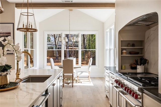 kitchen featuring decorative light fixtures, sink, dark stone counters, range with two ovens, and light hardwood / wood-style floors