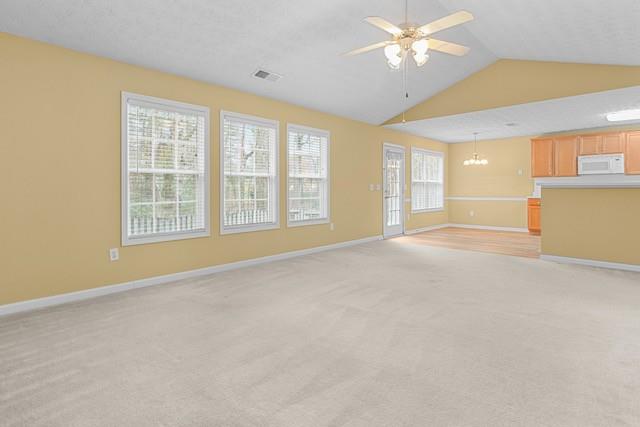 unfurnished living room with a wealth of natural light, light colored carpet, and ceiling fan with notable chandelier