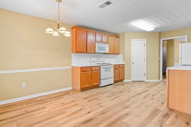 kitchen with light hardwood / wood-style flooring, a notable chandelier, pendant lighting, a textured ceiling, and white appliances