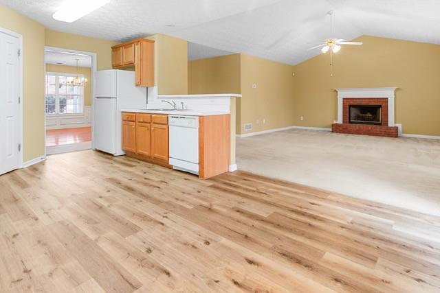 kitchen with lofted ceiling, white appliances, ceiling fan with notable chandelier, sink, and a brick fireplace