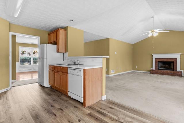 kitchen with a brick fireplace, white appliances, ceiling fan, sink, and light hardwood / wood-style floors