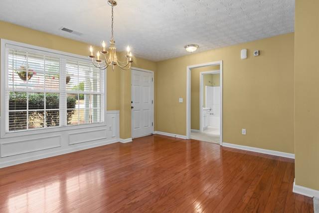 unfurnished dining area with wood-type flooring, a textured ceiling, and a notable chandelier