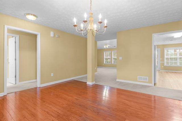 empty room featuring ceiling fan with notable chandelier, wood-type flooring, and a textured ceiling