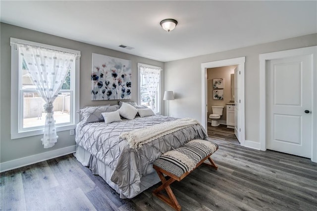 bedroom with connected bathroom, multiple windows, and dark wood-type flooring