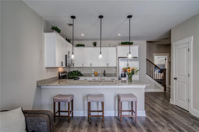 kitchen with white cabinets, appliances with stainless steel finishes, hanging light fixtures, and dark wood-type flooring