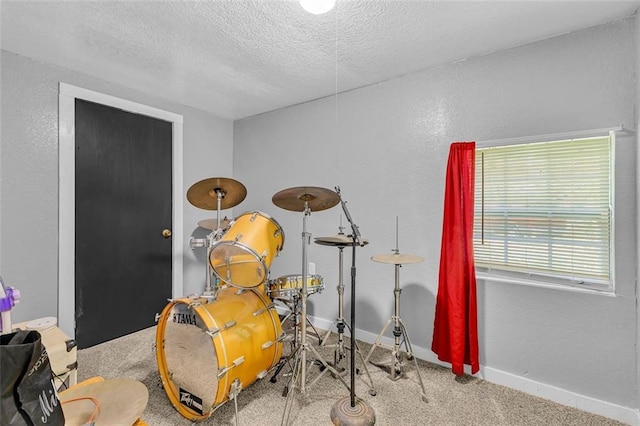 recreation room featuring a textured ceiling, carpet flooring, a textured wall, and baseboards