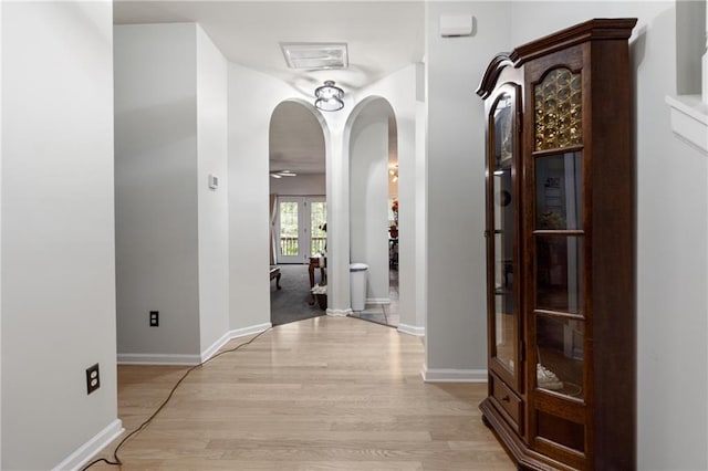 hallway featuring french doors, arched walkways, baseboards, and light wood-style flooring