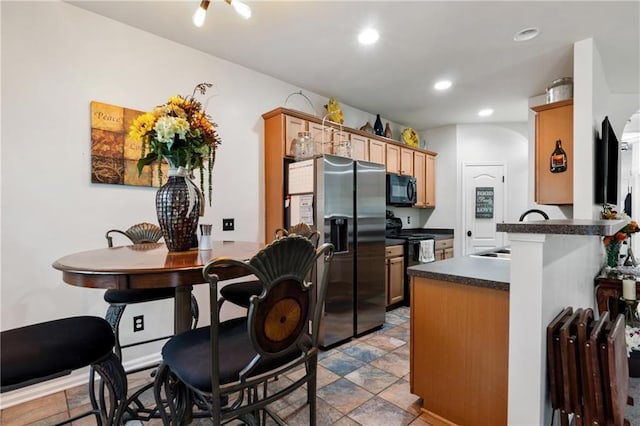 kitchen with stone finish flooring, dark countertops, a sink, black appliances, and recessed lighting