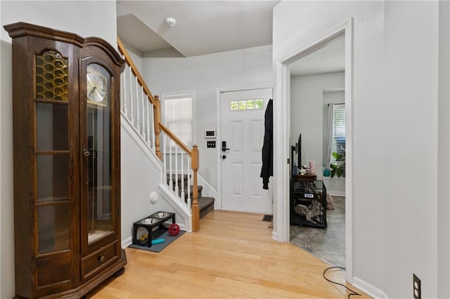 entryway featuring baseboards, light wood finished floors, and stairs