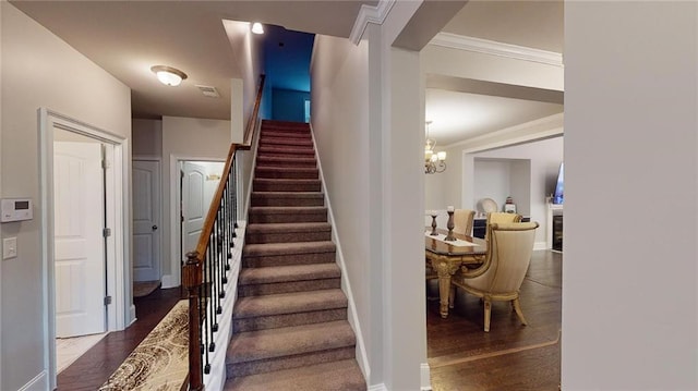 staircase with hardwood / wood-style floors, crown molding, and a notable chandelier