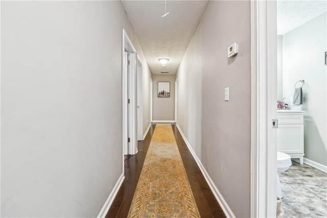 hall featuring baseboards, a textured ceiling, and wood finished floors