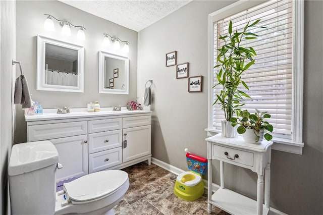 full bathroom featuring baseboards, double vanity, a sink, a textured ceiling, and toilet