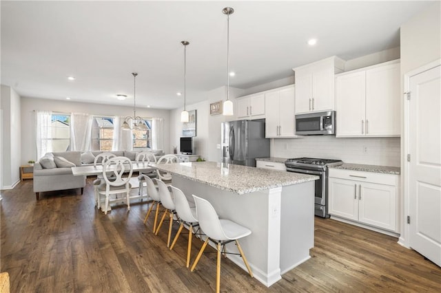 kitchen featuring a kitchen bar, white cabinetry, a center island, appliances with stainless steel finishes, and open floor plan
