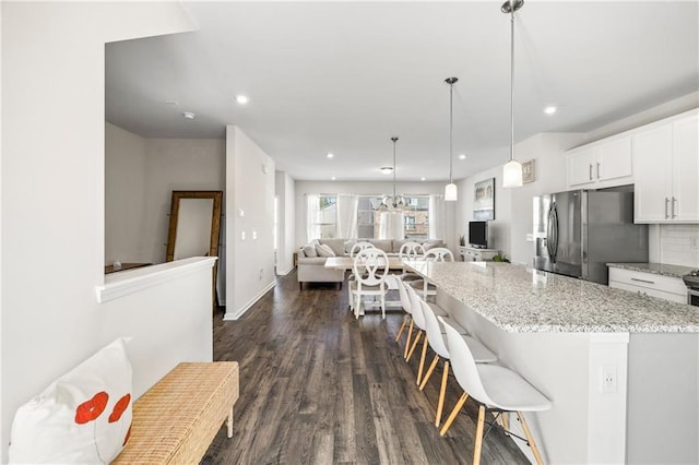 kitchen featuring stainless steel fridge, dark wood-style flooring, open floor plan, white cabinetry, and light stone counters
