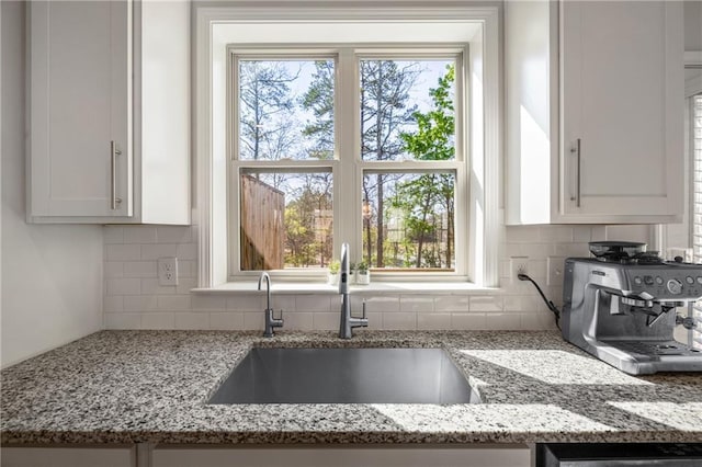 kitchen with a sink, decorative backsplash, a wealth of natural light, and light stone counters