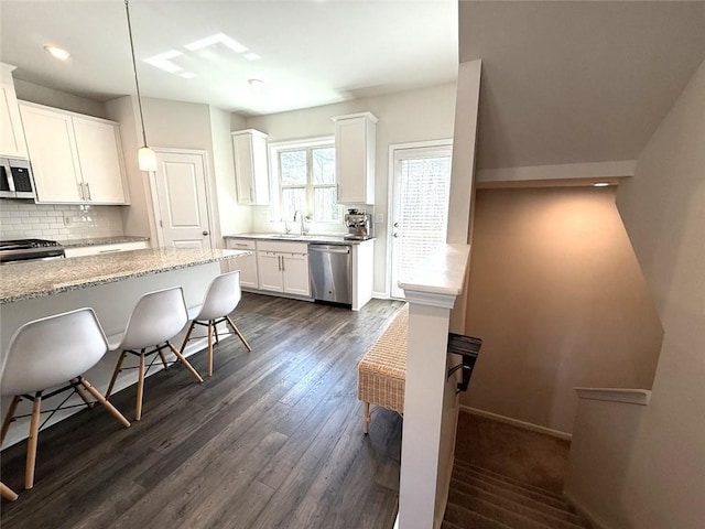 kitchen featuring appliances with stainless steel finishes, white cabinetry, light stone countertops, dark wood-type flooring, and backsplash