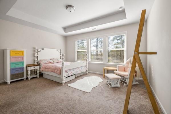 carpeted bedroom with a tray ceiling and baseboards