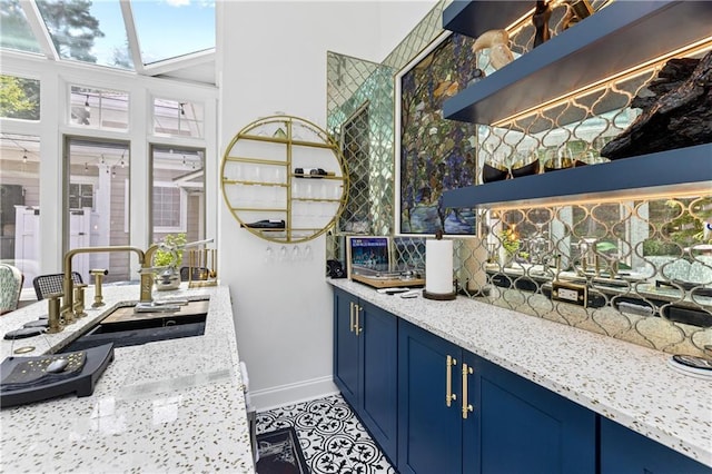 bar featuring light stone counters, blue cabinets, sink, and light tile patterned floors