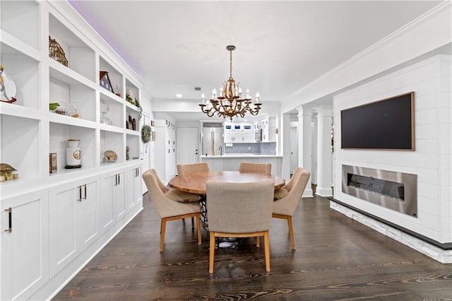 dining room with ornate columns, built in features, dark wood-type flooring, and an inviting chandelier