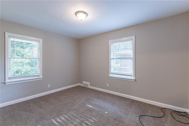 carpeted spare room with a healthy amount of sunlight, visible vents, and baseboards