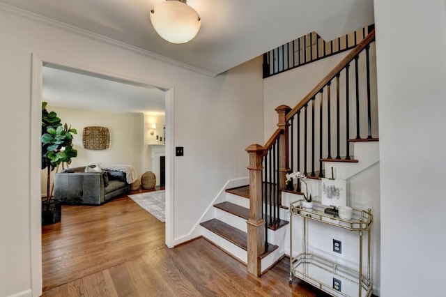 stairway with baseboards, wood finished floors, and crown molding