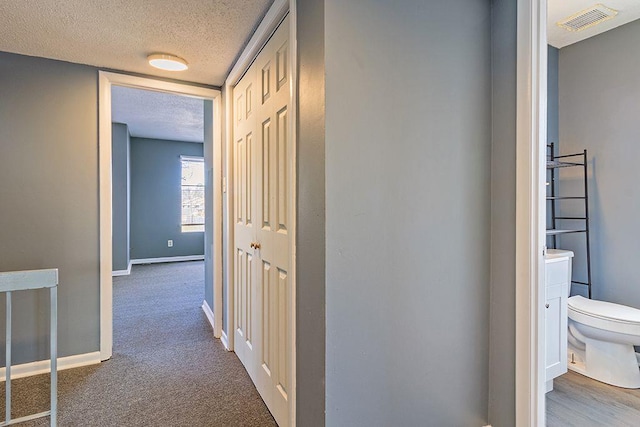 hallway with a textured ceiling and dark colored carpet