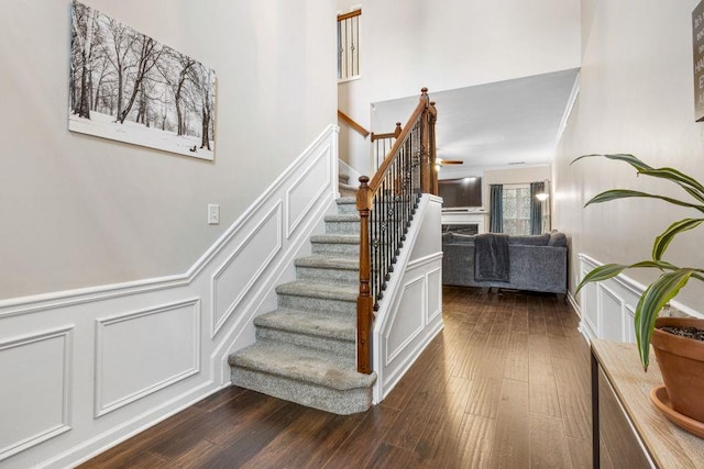 stairs featuring a decorative wall, a wainscoted wall, a fireplace, wood finished floors, and crown molding