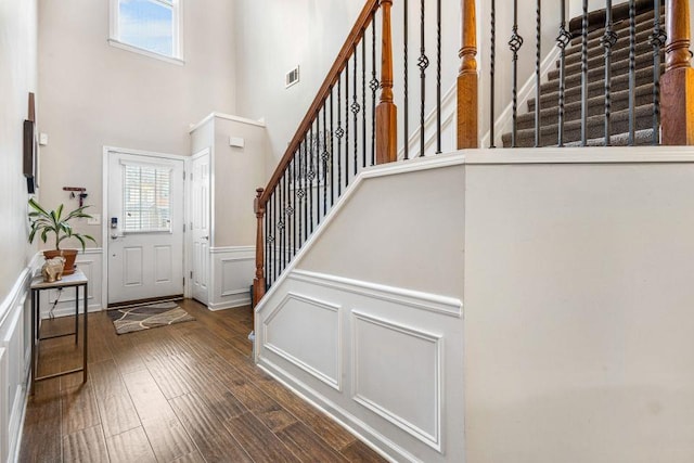 entryway featuring a decorative wall, a towering ceiling, wainscoting, wood finished floors, and stairs