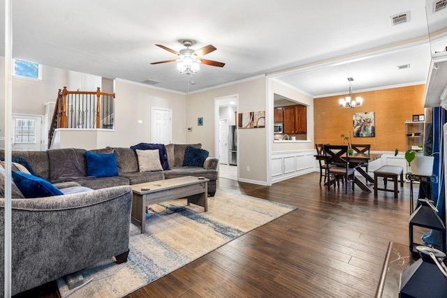 living area featuring dark wood-style floors, visible vents, ornamental molding, and ceiling fan with notable chandelier