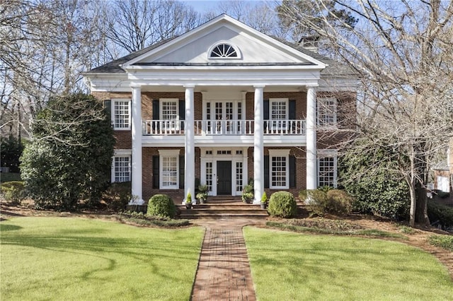 greek revival inspired property featuring brick siding, french doors, a front yard, and a balcony