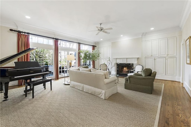 living area featuring ornamental molding, a warm lit fireplace, wood finished floors, recessed lighting, and ceiling fan