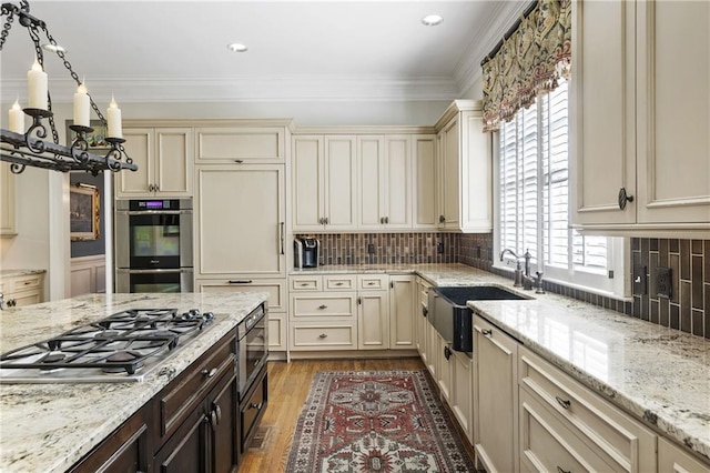 kitchen featuring light wood-type flooring, ornamental molding, a sink, cream cabinets, and appliances with stainless steel finishes