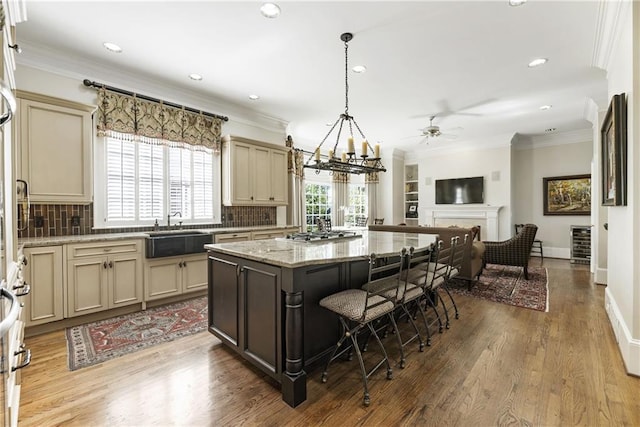 kitchen featuring cream cabinetry, ornamental molding, a breakfast bar, a sink, and open floor plan