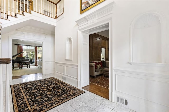 entryway with visible vents, crown molding, a decorative wall, a towering ceiling, and stairs