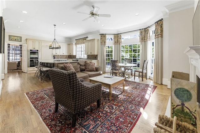 living area featuring recessed lighting, a fireplace, crown molding, ceiling fan with notable chandelier, and light wood-type flooring