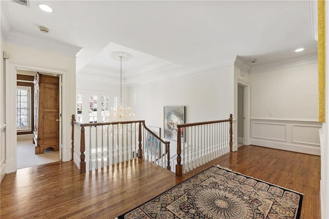 corridor featuring wood finished floors, ornamental molding, a decorative wall, a notable chandelier, and an upstairs landing