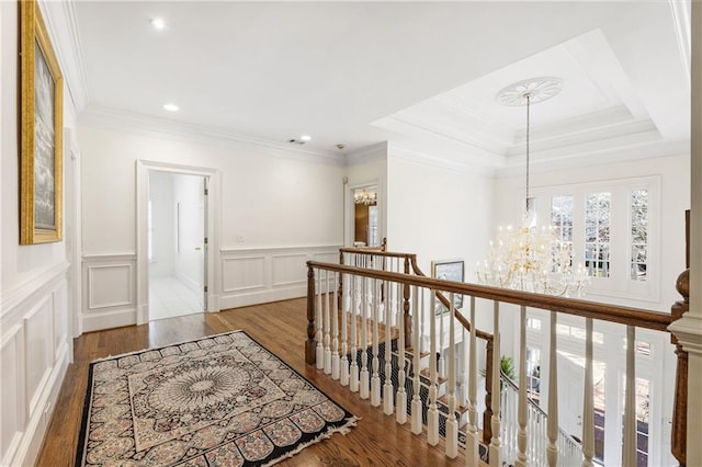 hall featuring crown molding, a chandelier, an upstairs landing, wood finished floors, and a decorative wall